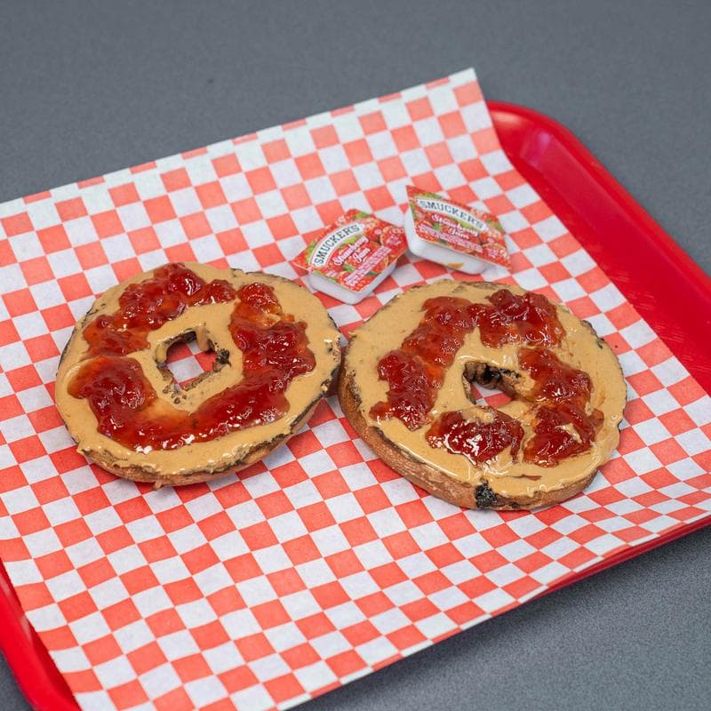 Peanut butter and jelly bagel on a tray lined with checkered paper.