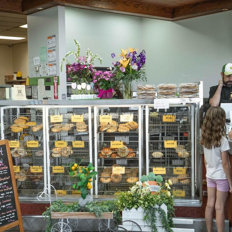 Assorted bagels arranged on stacked wire racks at a bakery counter.