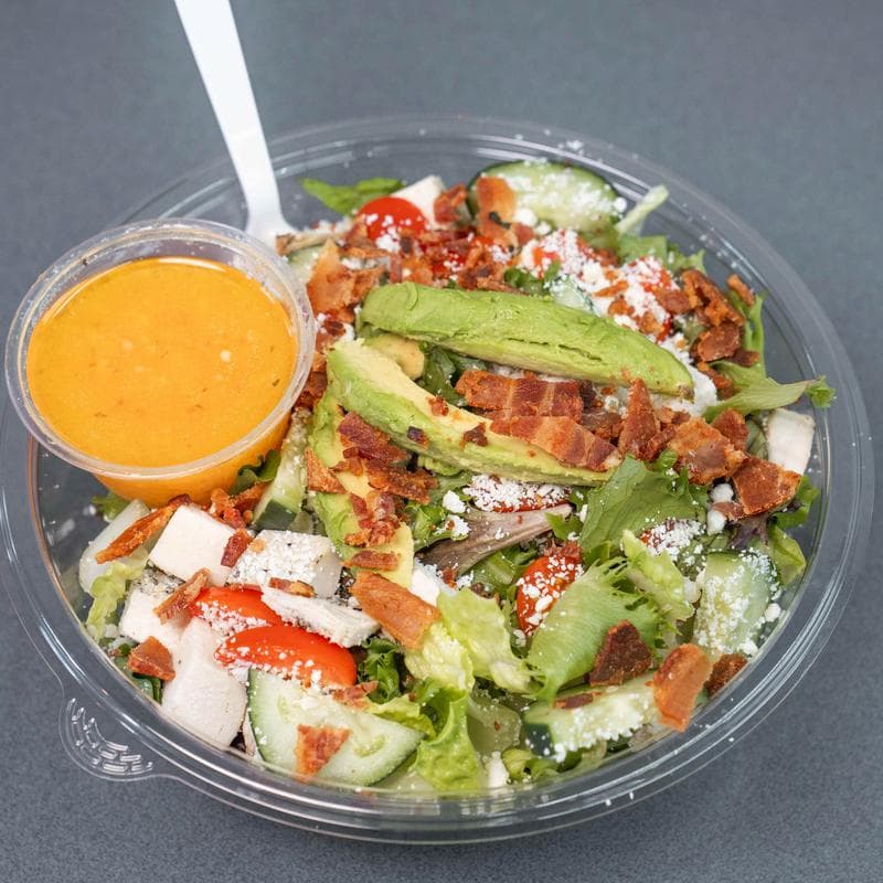 Cobb salad in a clear plastic container with a cup of Italian dressing.