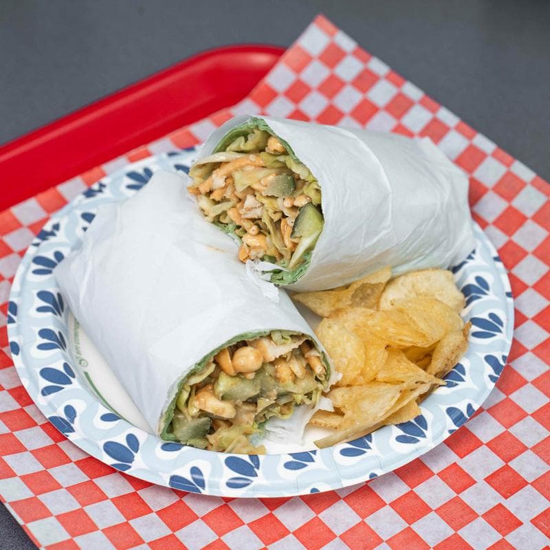 Thai chicken wrap served with potato chips on a patterned paper plate.
