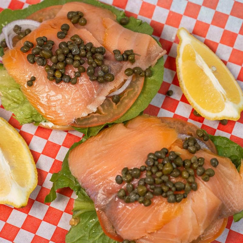 Smoked salmon bagel with capers, lettuce, and lemon wedges.